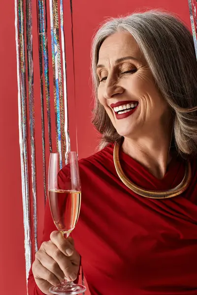 Una bella donna matura con i capelli grigi festeggia gioiosamente Natale e Capodanno con un bicchiere di champagne. — Foto stock