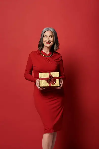 Una bella donna matura con i capelli grigi festeggia con gioia il Natale e il nuovo anno mentre tiene un regalo. — Foto stock