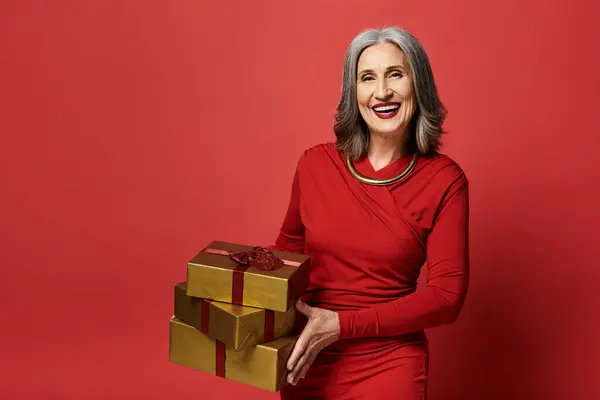 A radiant mature woman with grey hair joyfully embraces the holiday spirit while holding Christmas gifts. — Stock Photo