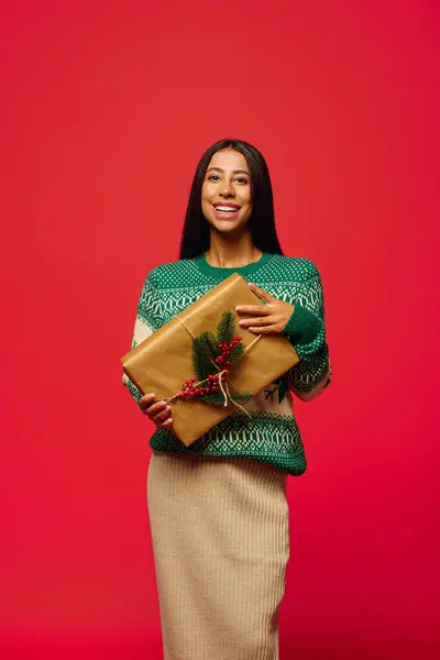 Une jeune femme joyeuse sourit brillamment tout en présentant un cadeau décoratif, rayonnant esprit de vacances. — Photo de stock