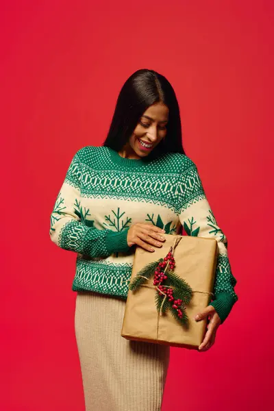 A cheerful young woman showcases her delight as she holds a beautifully wrapped holiday gift. — Stock Photo
