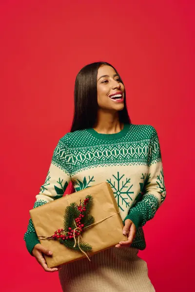 A joyful young woman smiles as she presents a beautifully wrapped gift for the holidays. — Stock Photo