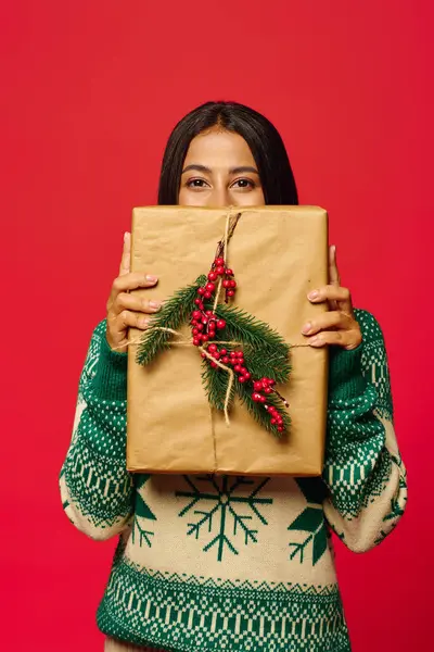 Una giovane donna allegra copre il suo sorriso con un regalo di festa ornato di verde. — Foto stock
