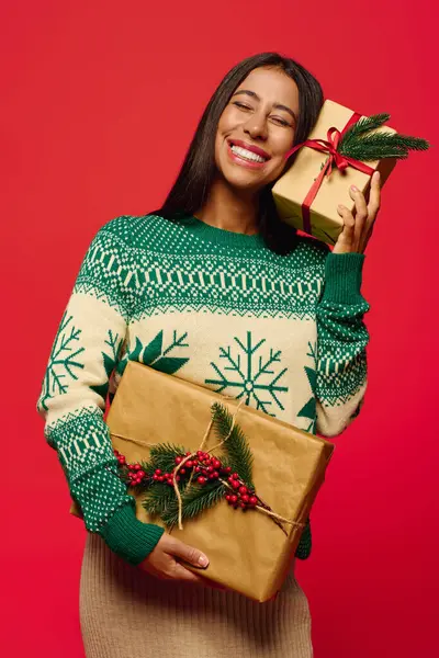 A joyful young woman poses with wrapped gifts against a bright red backdrop. — Stock Photo