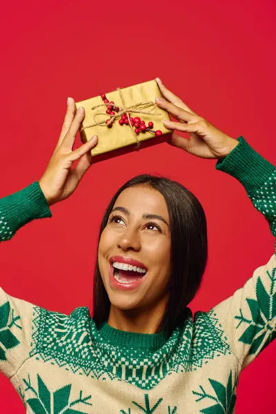 The young woman beams with happiness while lifting a wrapped gift high, radiating festive cheer. — Stock Photo