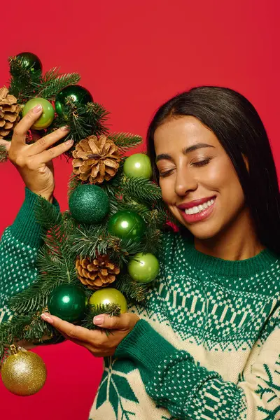 Una joven alegre sostiene una hermosa guirnalda adornada con adornos, sonriendo brillantemente. - foto de stock