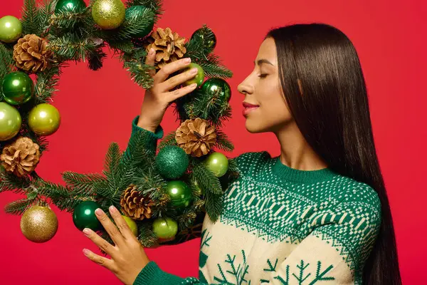 The beautiful woman gently holds a decorated wreath adorned with ornaments and pinecones. — Fotografia de Stock