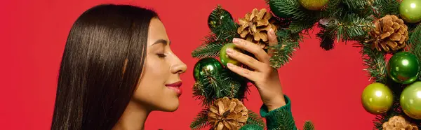 A young woman joyfully adorns a green wreath with shiny ornaments while smiling. — Stock Photo