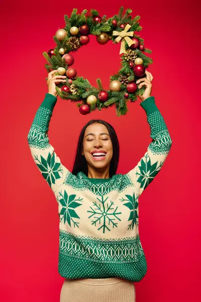 The young woman beams with happiness as she lifts a vibrant holiday wreath in celebration. — Stock Photo