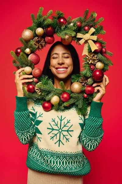 A joyful young woman holds a colorful Christmas wreath full of ornaments. — Stock Photo