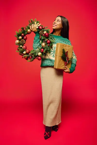 Eine lächelnde Frau steht in einem kuscheligen Pullover und feiert die Weihnachtszeit mit Geschenken. — Stockfoto