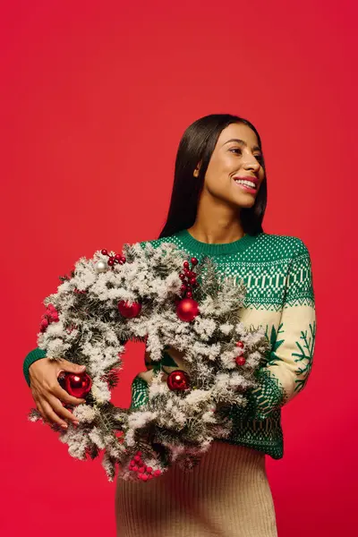 A cheerful woman displays a beautifully decorated wreath, embodying holiday spirit and joy. — Stock Photo