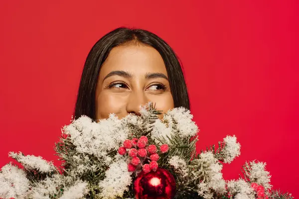 A cheerful young woman peeks over a beautiful arrangement of holiday decorations, smiling. — Stock Photo