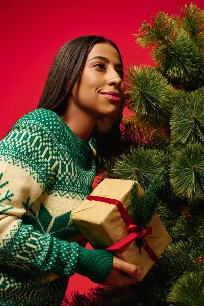 The young woman smiles as she holds a beautifully wrapped present near a vibrant Christmas tree — Stock Photo