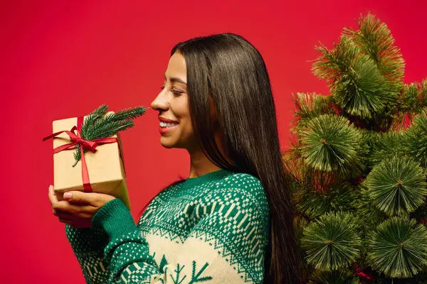A young woman with long hair displays a cheerful smile while presenting a beautifully wrapped gift. — Stock Photo