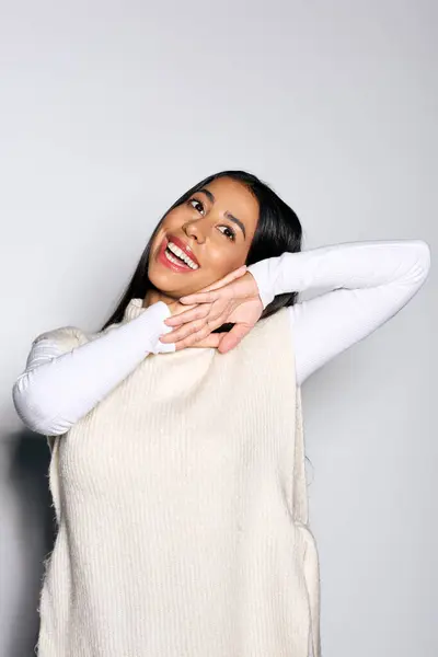 Una mujer joven con largas vigas de pelo con alegría, mostrando su sonrisa radiante en un suéter de punto. - foto de stock
