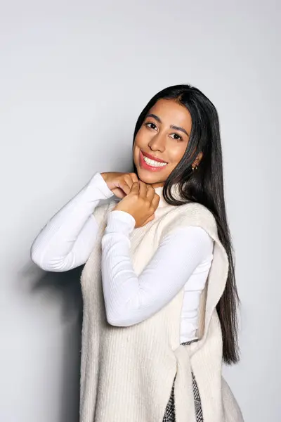 The cheerful young woman smiles warmly while adjusting her outfit in a cozy atmosphere. — Stock Photo