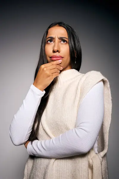 A young woman in a soft sweater ponders deeply, lost in thoughtful reflection within a calm setting. — Stock Photo