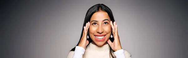 A cheerful young woman smiles broadly while touching her face, radiating joy and warmth. — Stock Photo