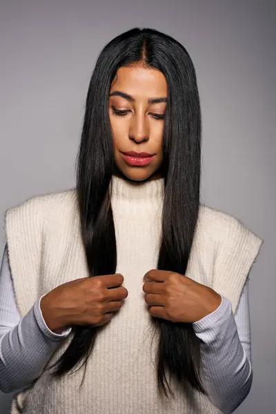A young woman in a stylish sweater gently touches her long, straight hair while closing her eyes. — Stock Photo