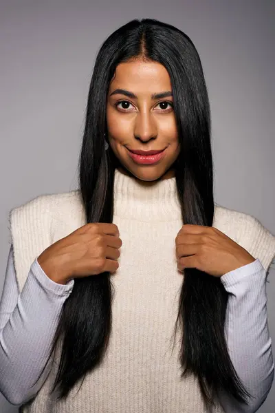 The young woman showcases her long hair while wearing a stylish sweater, smiling gently. — Stock Photo