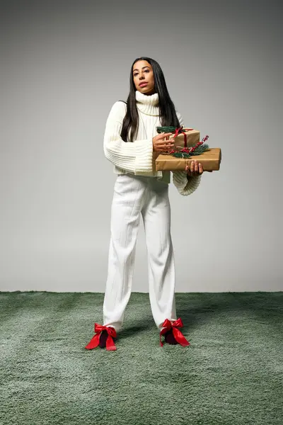 A stylish young woman with a serene expression holds colorful, festive holiday gifts. — Stock Photo