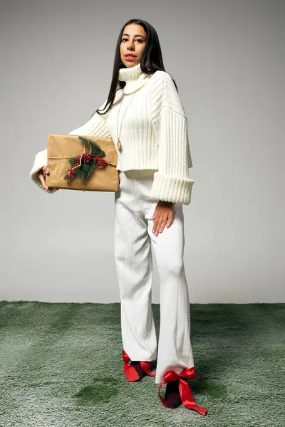 A chic young woman poses elegantly in her stylish winter outfit, holding a gift. — Stock Photo