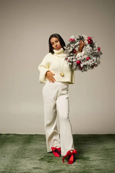 Une jeune et belle femme présente une couronne festive vêtue d'une tenue d'hiver chic. — Photo de stock