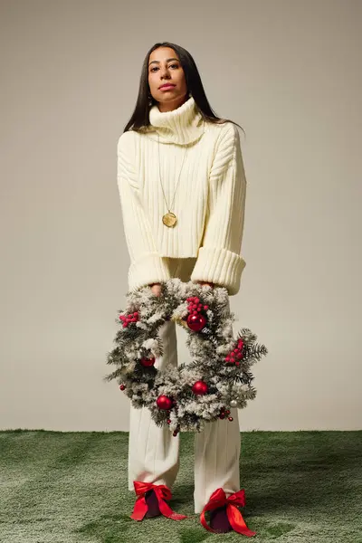 A young, beautiful woman poses gracefully while holding a decorative wreath adorned with ornaments. — Stock Photo