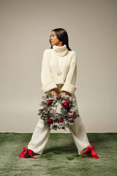The woman stands confidently, showcasing a holiday wreath adorned with red accents. — Stock Photo