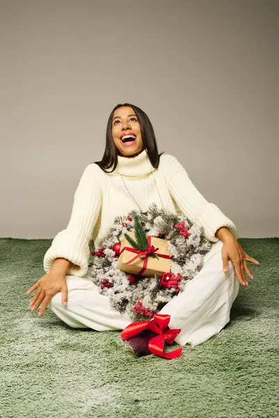 Uma jovem mulher feliz senta-se no chão, abraçando decorações festivas e presentes com alegria. — Fotografia de Stock