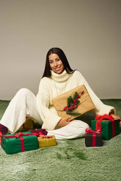 Radiating joy, a young woman dons a cozy sweater while celebrating the festive season with gifts. — Stock Photo