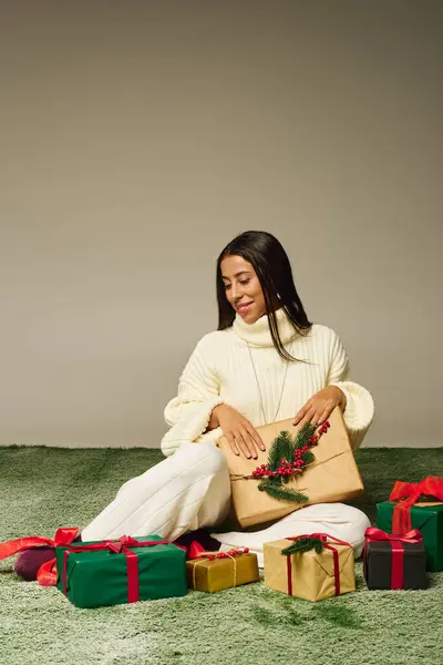 Una hermosa mujer sonríe mientras abre un regalo rodeado de coloridos regalos navideños.. - foto de stock