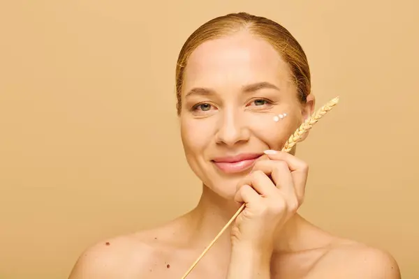 A young woman with a glowing complexion gently applies skincare while holding a natural element. — Stock Photo