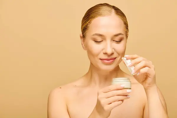 A young, confident woman delights in applying cream to enhance her natural beauty during self care. — Stock Photo