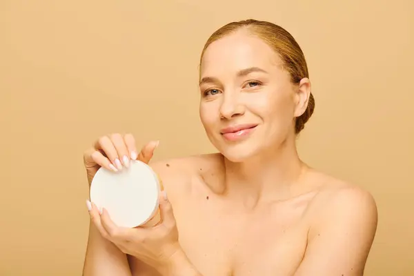 A confident young plus size woman smiles while holding a skincare item close to her face. — Foto stock