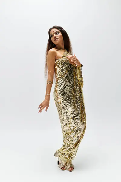 A stunning goddess exudes confidence in a shiny gold dress, striking a captivating pose in a modern studio. — Stock Photo