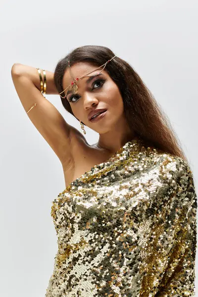 The radiant goddess in a golden dress poses gracefully, showcasing elegance and confidence in the studio. — Stock Photo