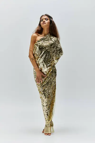 A beautiful figure poses gracefully in a shiny golden dress, exuding elegance in a calm studio atmosphere. — Stock Photo