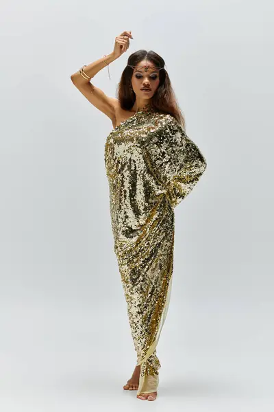 A mesmerizing African American goddess stands gracefully, showcasing her shiny golden dress in a stylish studio setup. — Stock Photo
