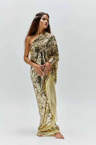 A radiant figure adorned in a shiny golden dress stands confidently against a neutral backdrop. — Stock Photo