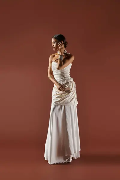 A beautiful African American woman showcases grace wearing a white dress and a pearl necklace in a studio. — Fotografia de Stock