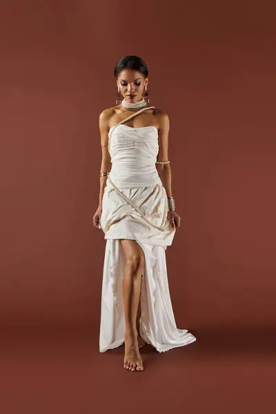 Elegant African American woman in a pearl-adorned white dress stands out against a brown backdrop. — Stock Photo