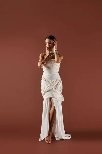 A gorgeous African American woman in a white dress and pearls poses elegantly against a warm brown backdrop. — Stock Photo