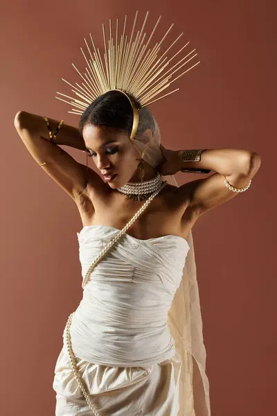 An elegant African American woman poses in a pearl-embellished white dress against a warm brown background. — Stock Photo