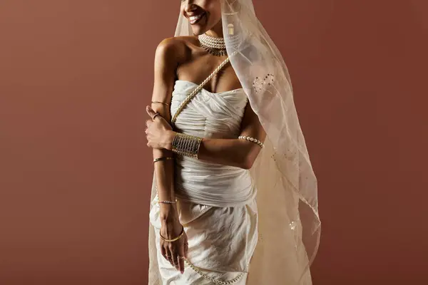 Uma mulher afro-americana deslumbrante usa um vestido branco e pérolas, incorporando elegância contra um pano de fundo quente. — Fotografia de Stock