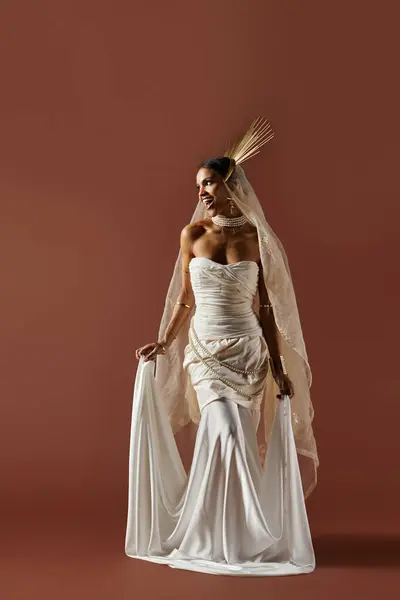 An elegant woman dressed in white with a pearl necklace strikes a regal pose against a warm background. — Stock Photo