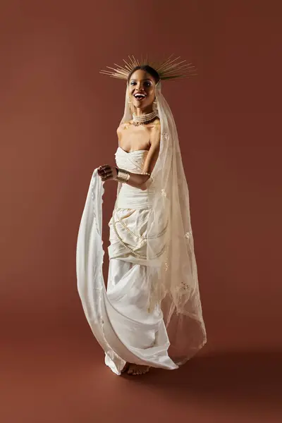 A stunning African American woman gracefully poses in a white dress, adorned with pearls against a warm backdrop. — Stock Photo