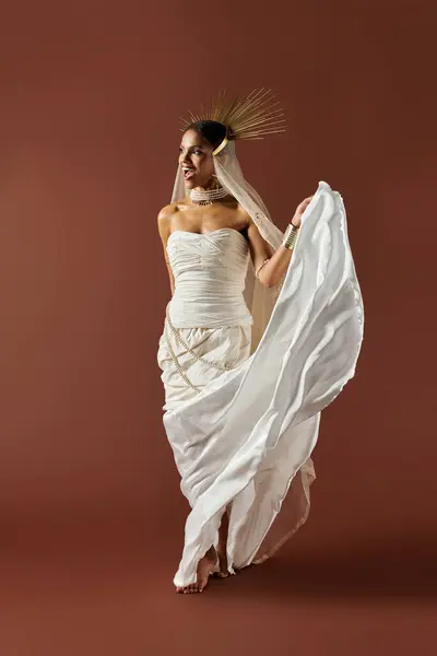 A stunning African American woman in a flowing white dress and pearl necklace radiates elegance in a studio. — Stock Photo