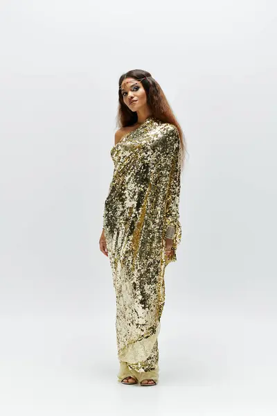 A radiant figure in a golden gown captivates in a minimalist studio, exuding elegance and beauty. — Stock Photo